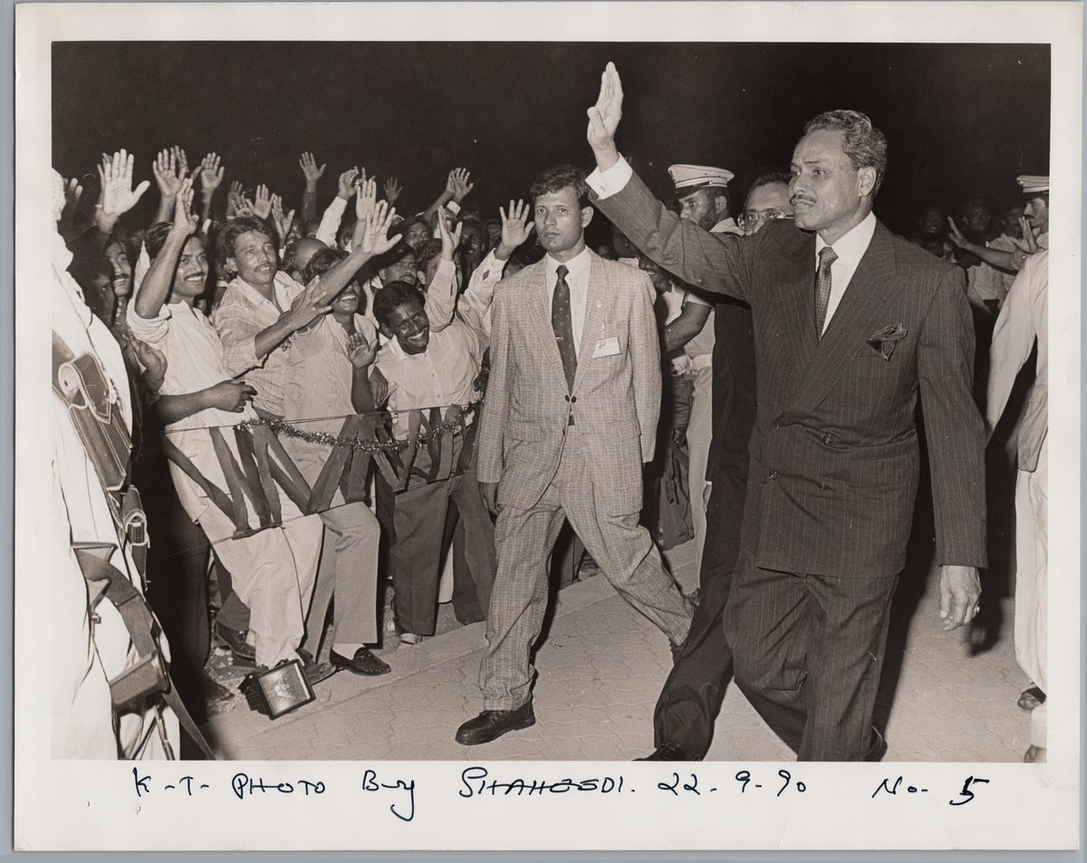 A Suited Visitor Waves to a Welcoming Crowd — front